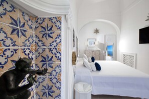 A bedroom with a bed, white walls, and a decorative tile wall. - Estate4home - Regina Dar (Positano)