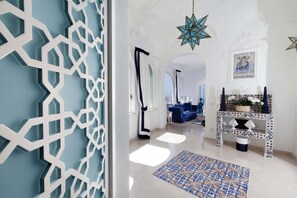 A hallway with a geometric white wall design, a blue patterned rug, and a star-shaped hanging light. - Estate4home - Regina Dar (Positano)