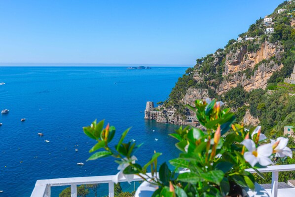 A coastal view with a clear blue sea, boats, and a rocky cliff with buildings. - Estate4home - Regina Dar (Positano)