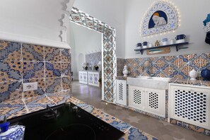 A kitchen with patterned tiles, a black stove, white cabinets, and a decorative wall piece. - Estate4home - Regina Dar (Positano)