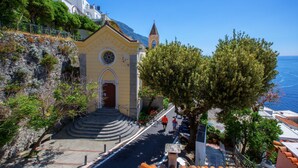 Una iglesia costera con un campanario, escalones que conducen a la entrada y vistas al mar.