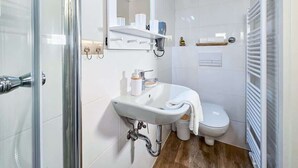 Un bany modern amb plat de dutxa de vidre, un lavabo blanc amb mirall i un vàter amb barra de tovalloles.