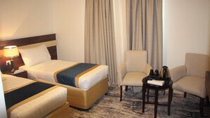 A hotel room with two beds, a chair, a small table, and a lamp. - Burj Mawaddah Hotel (Madinah)