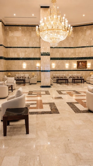A lobby with a large chandelier, marble walls, and multiple seating areas.