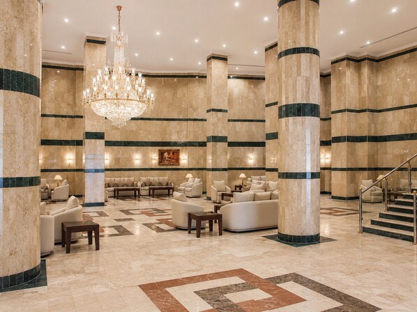 A spacious lobby with high ceilings, large columns, a grand chandelier, and multiple seating areas.