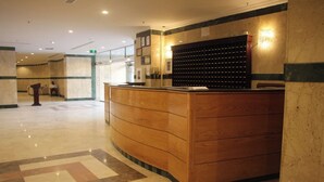A reception desk with a wooden finish, a wall-mounted telephone, and a bulletin board. - Burj Mawaddah Hotel (Madinah)