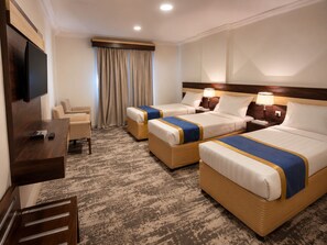 A hotel room with three beds, a TV, a desk, and a chair.