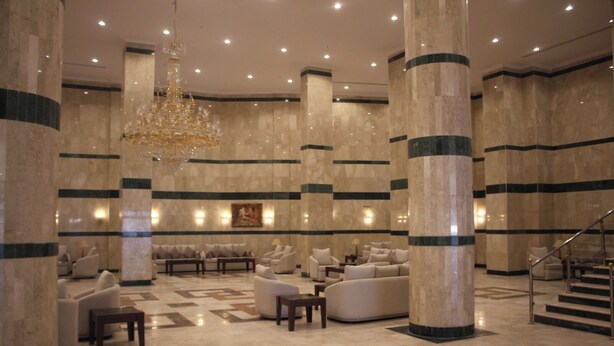 A spacious lobby with high ceilings, large columns, and a grand chandelier. There are multiple seating areas with sofas and armchairs. - Burj Mawaddah Hotel (Madinah)