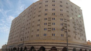 A large, multi-story building with a curved facade, featuring a series of windows and a central entrance. - Burj Mawaddah Hotel (Madinah)