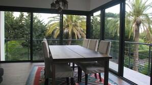 A dining area with a large table and chairs, large windows with a view of palm trees, and a hanging light fixture. - VILLA LA MASCOTTE PLUS IN CANNES (Cannes)