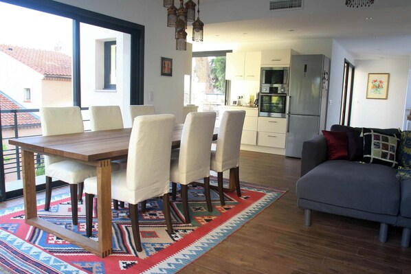 A dining area with a wooden table and chairs, a patterned rug, and a grey sofa.