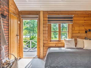 A wooden cabin room with a bed, a fireplace, and a view of trees.