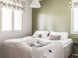 A bedroom with a bed, pillows, a blanket, and a bedside table with a vase.