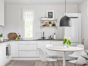 A modern kitchen with white cabinetry, a round dining table with white chairs, and a pendant light.