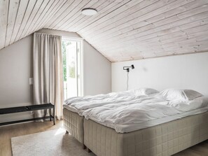 A bedroom with a sloped ceiling, a bed, a bedside table, and a window with curtains.