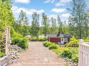 A gravel driveway leading to a red building with a white door, surrounded by greenery and trees.