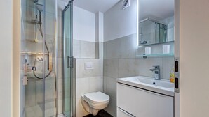Un baño moderno con ducha de vidrio, inodoro y lavamanos con espejo.