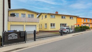 Una hilera de edificios residenciales de dos pisos, con balcones, un camino de entrada con portón y coches aparcados.