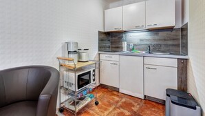 Una cocina compacta con armarios blancos, microondas, tostadora y un lavamanos pequeño.