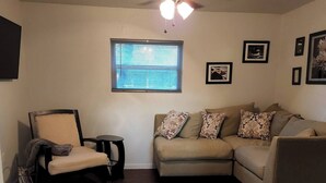 Un salon avec un canapé beige, un tapis à motifs, un ventilateur de plafond et des tableaux encadrés accrochés au mur.