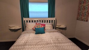 Un lit avec une tête de lit blanche et une couvre-lit matelassée, deux tables de chevet et une fenêtre ornée de rideaux turquoise.