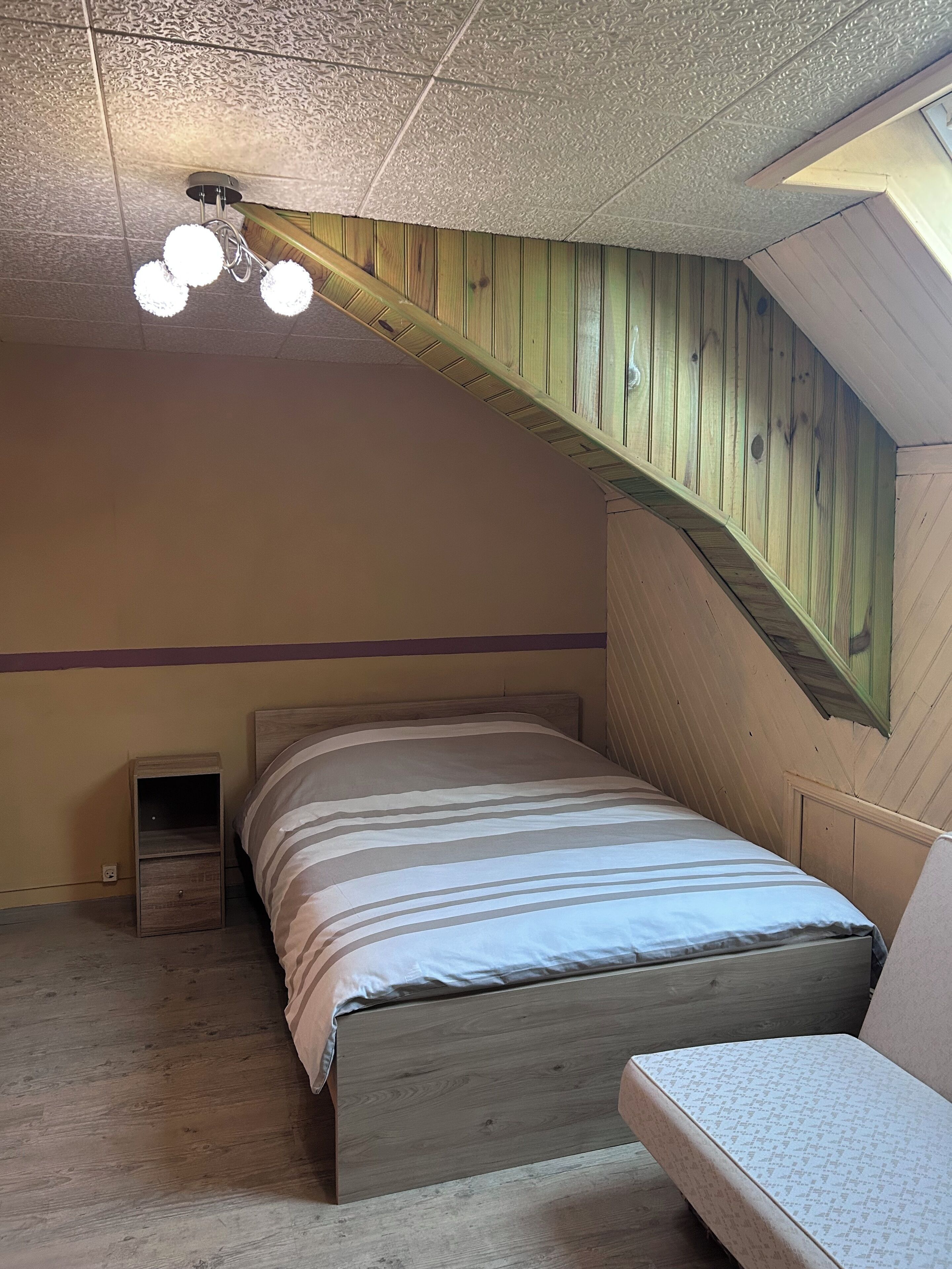 A bedroom with a sloped ceiling, a bed with striped bedding, a nightstand, and a small window.