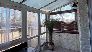 Aurinkoinen huone, jossa on suuret ikkunat, ruukkuistutettu kasvi ja musta viihdekeskus.