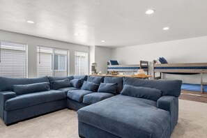 A room with a sectional sofa, a bunk bed, and a desk with a chair.