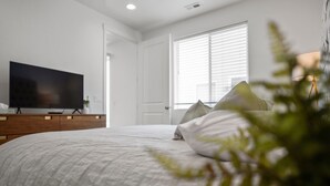 Un dormitorio con una cama, un televisor sobre un mueble, una puerta y una ventana con persianas.