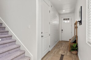 A hallway with a staircase, white doors, a wooden bench, and a potted plant. - Valley Views | Bear Lake Marina | King Suite + BBQ (Garden City)