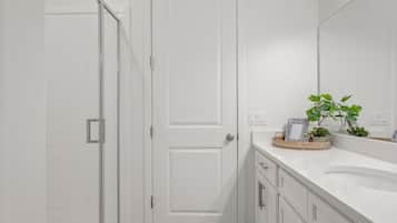 Une salle de bain blanche avec une porte fermée, un meuble-lavabo avec un miroir et une petite plante posée sur le comptoir.