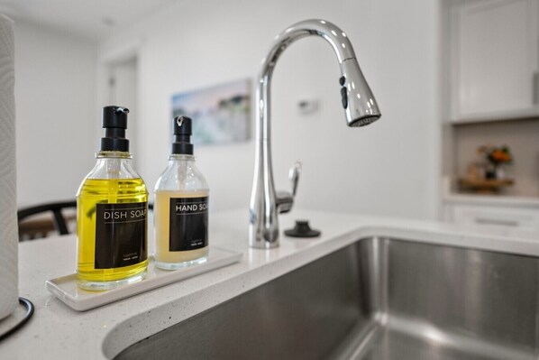 Une cuisine avec un évier en acier inoxydable, deux bouteilles de liquide vaisselle et un flacon de savon pour les mains posés sur le comptoir.
