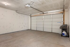 Un garage avec un plancher en béton, une porte de garage blanche et une cuve de propane situ ée à droite.