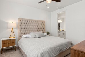 Une chambre à coucher avec une tête de lit capitonnée, une lampe de chevet, une table de chevet en bois, un lit avec une literie blanche et une commode en bois.