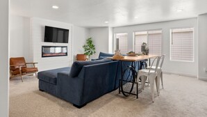 Una sala de estar moderna con un sofá modular, una chimenea, una mesa de comedor con sillas y un televisor montado en la pared.