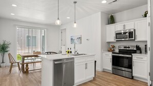 Una cocina moderna con armarios blancos, electrodomésticos de acero inoxidable e iluminación colgante.
