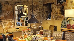 Un comedor rústico con pared de piedra, sillas de mimbre, una mesa de madera dispuesta para una comida y una lámpara colgante.