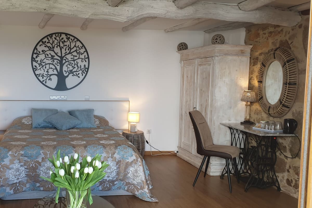 A bedroom with a bed, bedside lamps, a chair, a desk, a mirror, and a vase of tulips.