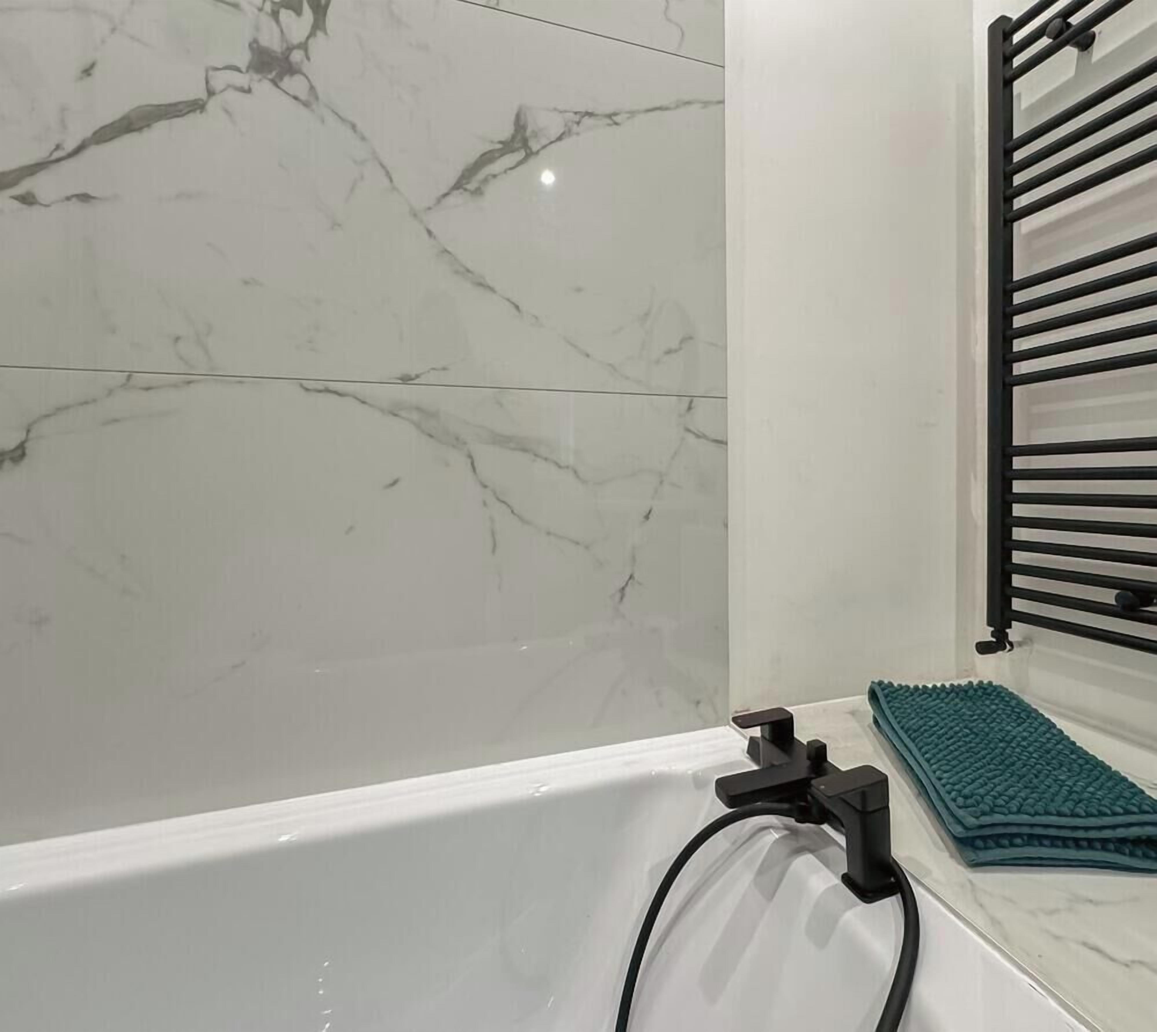 Ein Badezimmer mit einer Badewanne, einem Handtuchhalter und einer grünen Fußmatte.
