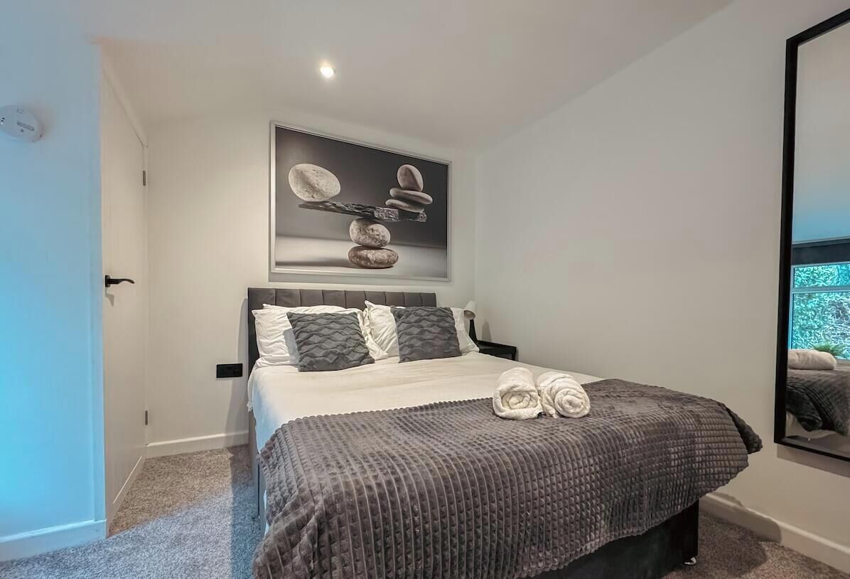 Een slaapkamer met een bed, kussens, een dekbed, een kunstwerk aan de muur en een spiegel.