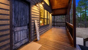 Une cabane en bois avec un porche, une pancarte de bienvenue et un espace abrité doté de fenêtres.