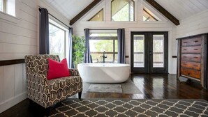 Une pièce spacieuse avec une grande baignoire, un fauteuil à motifs et une commode en bois.