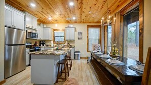A modern kitchen with a central island, stainless steel appliances, and a wooden ceiling.