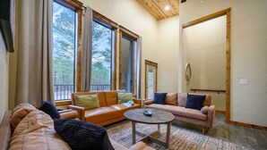 A cozy living room with a sofa, two armchairs, a coffee table, and large windows offering a view of trees.