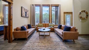 A spacious living room with a large window, a ceiling fan, and a wooden ceiling.