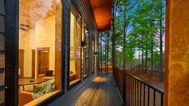 A wooden deck with a railing, large windows, and a view of trees.