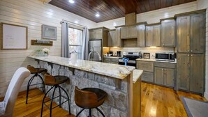 A kitchen with wooden cabinets, a granite countertop, and a stone island with bar stools. - Merlot Mountain • Pool, Hottub, Firepit, Fireplace (Broken Bow)