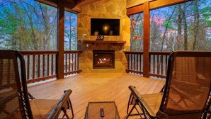 A covered deck with a stone fireplace, a flat-screen TV, and wicker chairs. - Merlot Mountain • Pool, Hottub, Firepit, Fireplace (Broken Bow)