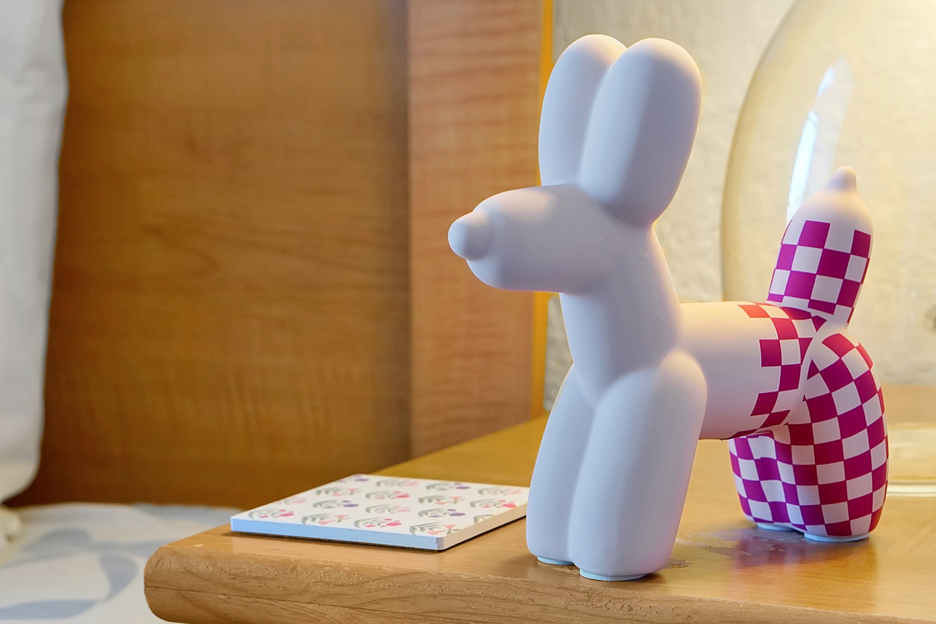 Eine weiße Kaninchenfigur auf einer Holzoberfläche, neben einem Schachbrettmuster-Objekt.
