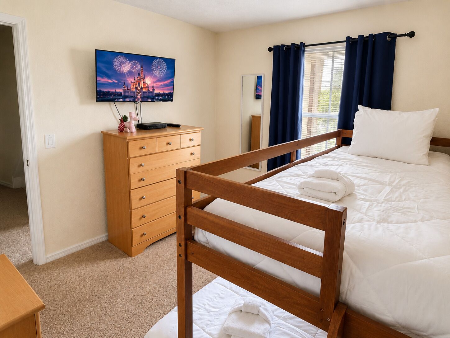 Ein Schlafzimmer mit einem hölzernen Bettgestell, einem Schminktisch, einem Flachbildfernseher und einem Fenster mit Vorhängen.
